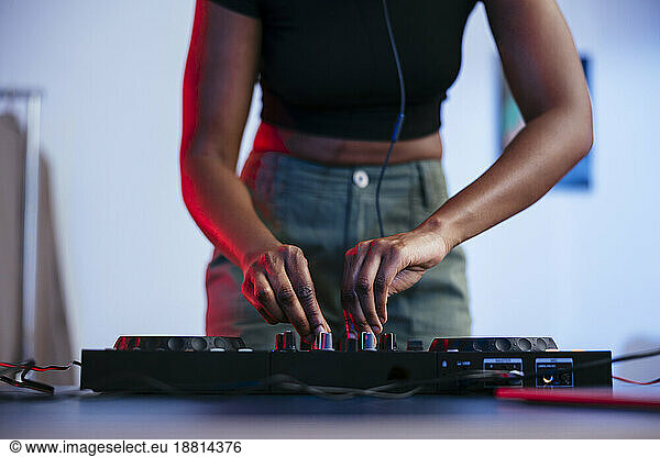 Young female Dj operating sound mixer at home