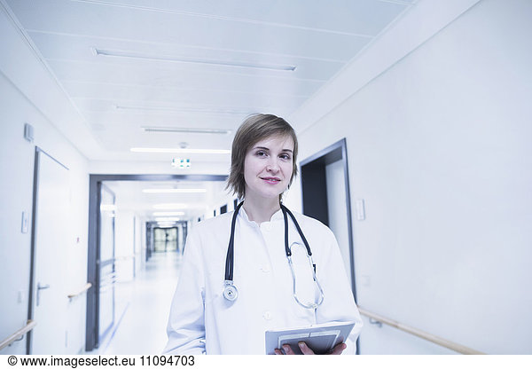 Young female doctor holding clipboard in hospital corridor