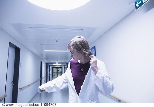 Young female doctor looking at her hand while walking in hospital corridor