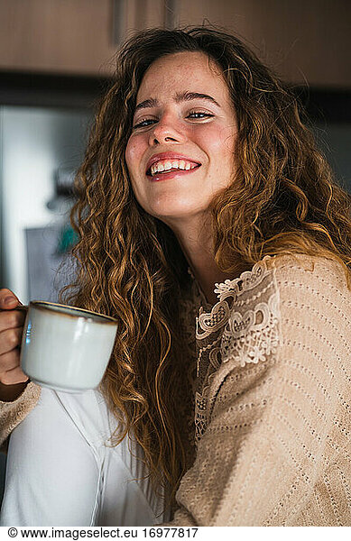 Young female drinking hot beverage and smiling to camera