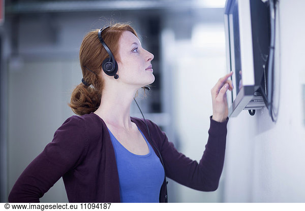 Young female engineer wearing headset and working on touchscreen computer monitor in an industrial plant