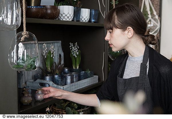 Young female entrepreneur arranging decorations on shelf at store