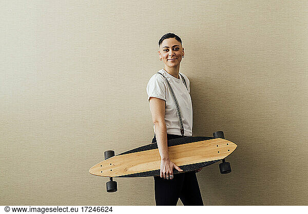 Young female entrepreneur holding skateboard while leaning on wall