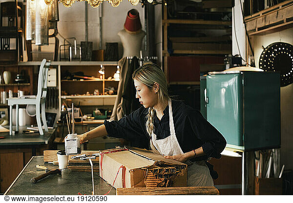 Young female entrepreneur working at workbench in workshop
