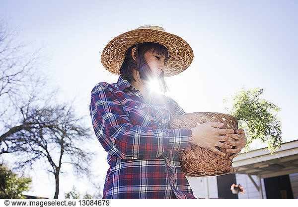 Young female farmer carrying basket in farm during sunny day