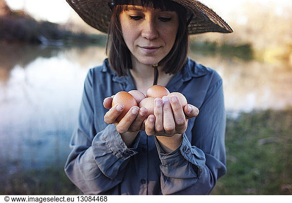 Young female farmer holding eggs while standing on lakeshore