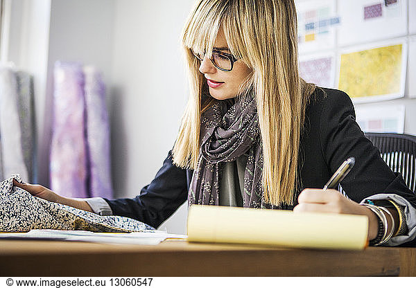 Young female fashion designer checking fabric on desk