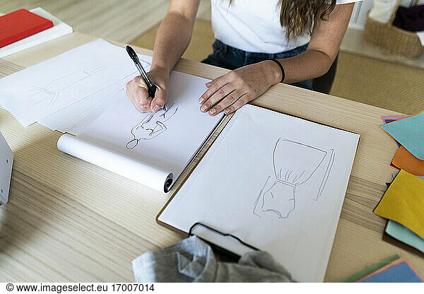 Young female fashion designer sketching design in book at studio