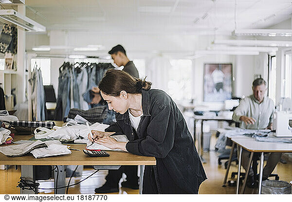 Young female fashion designer writing on package while working at workshop