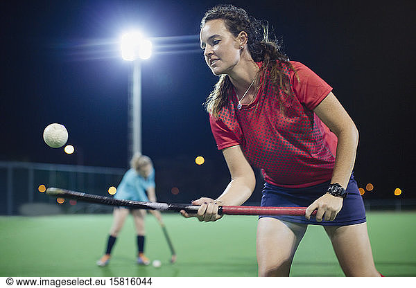 Young female field hockey player bouncing ball off hockey stick  practicing on field at night