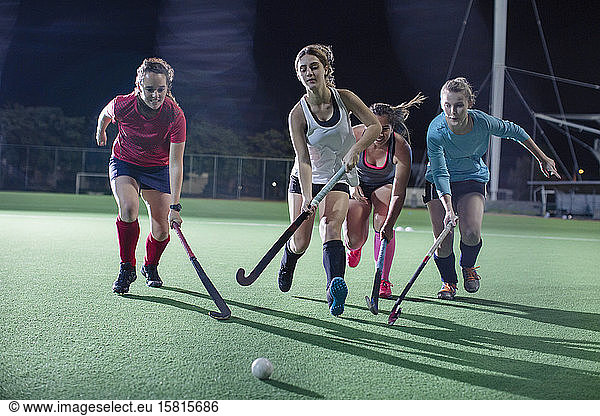 Young female field hockey players running for the ball  playing on field at night