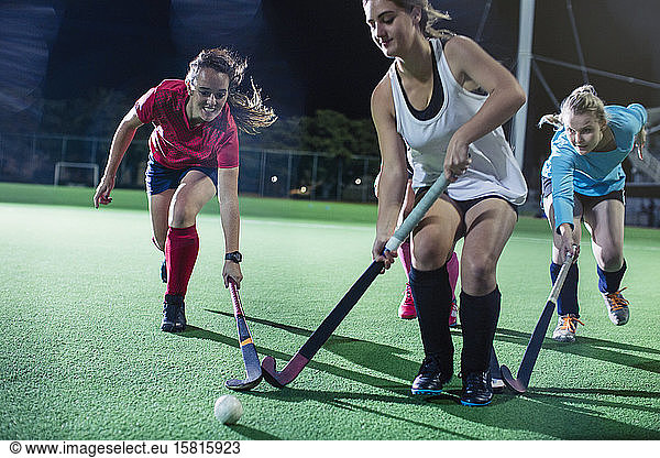 Young female field hockey players running to ball  playing field hockey on field at night