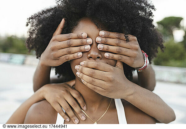 Young female friends covering mouth and eyes of Afro woman