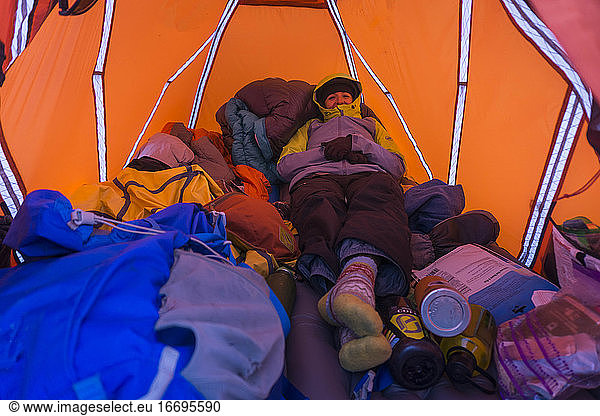 Young female hiker in warm clothing resting in tent