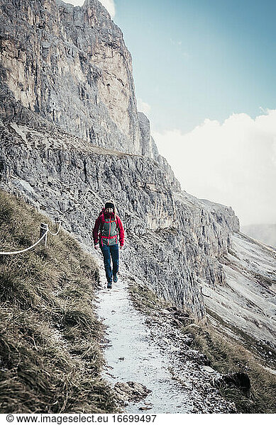 Young female hiking on trail next to steep mountain face in Dolomites