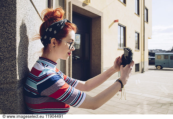 Young female hipster taking selfie while standing against wall