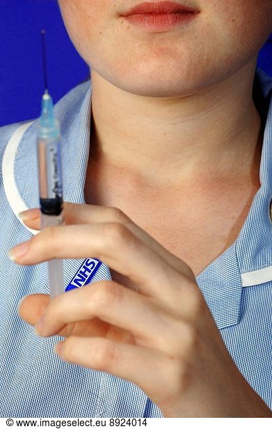 Young female nurse holding a hypodermic syringe containg a clear solution.