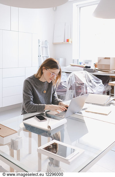 Young female owner using laptop at desk in workshop