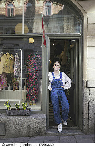 Young female owner with hand on hip standing at doorway of boutique