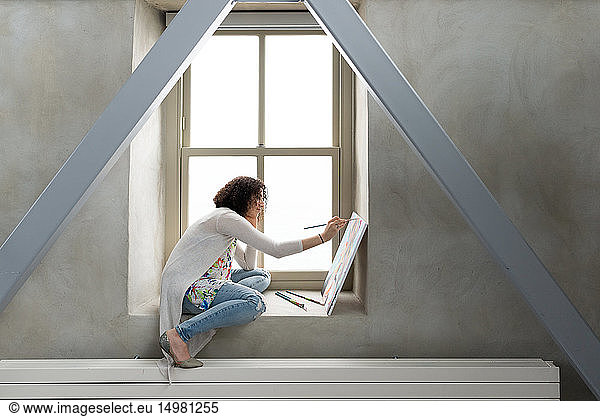 Young female painter painting canvas on studio windowsill