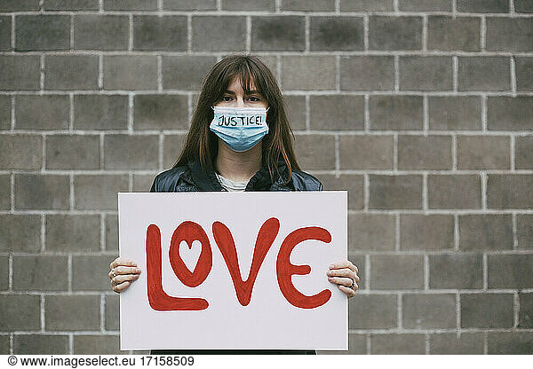 Young female protestor with love poster against wall during pandemic