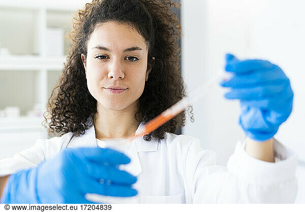 Young female researcher mixing solution in beaker through pipette at chemistry lab