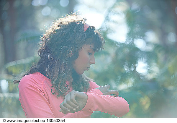 Young female runner putting on armband in sunlit forest
