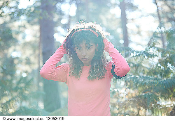 Young female runner putting on headphones in sunlit forest