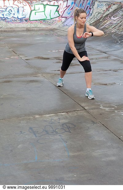Young female runner warming up and checking stop watch in skatepark