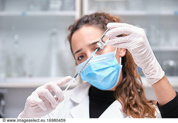 Young female scientist wearing face mask holding a coronavirus vaccine vial  syringe and needle. Covid-19 vaccine development.young  female  scientist  wearing  face  mask  holding  coronavir