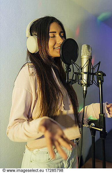 Young female singer with eyes closed gesturing while singing at studio