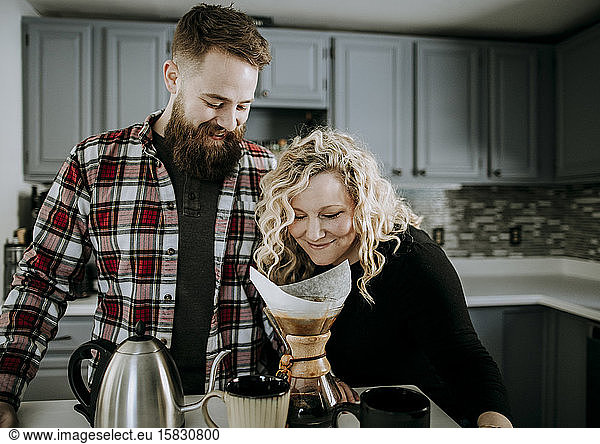 young female smells morning coffee while husband with beard looks on