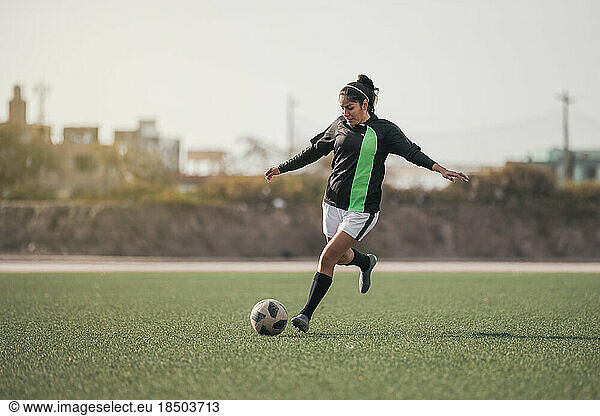 Young female soccer player kicking ball.