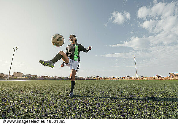 Young female soccer player kicking ball in a stadium.