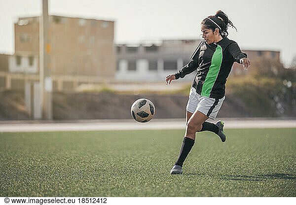 Young female soccer player kicking ball in a stadium.