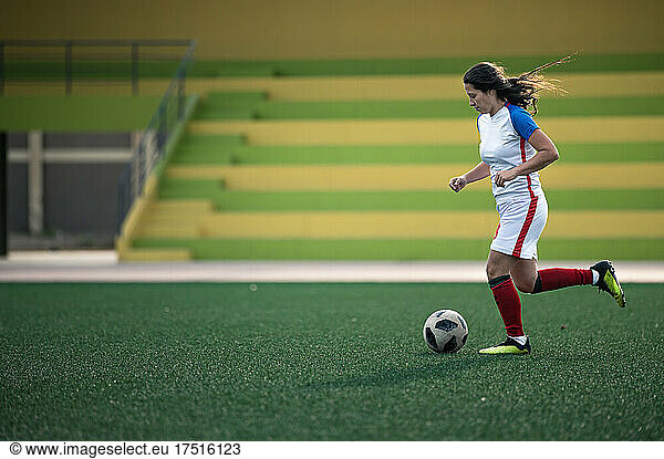 Young female soccer player kicks the ball on the field