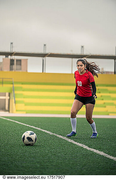 Young female soccer player kicks the ball on the field