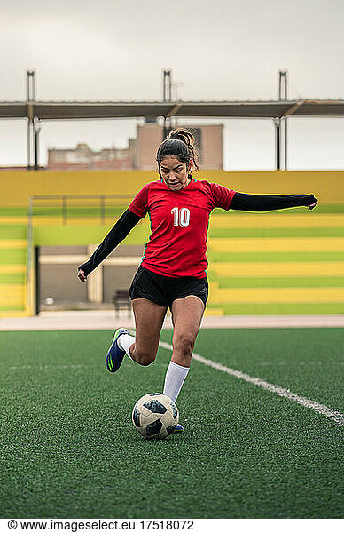 young female soccer player kicks the ball on the field