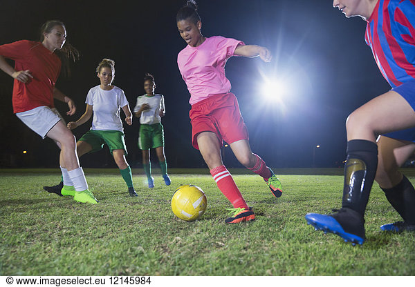 Young female soccer players playing soccer on field at night