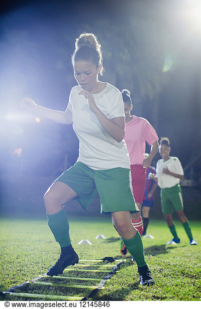 Young female soccer players practicing agility sports drill on field at night