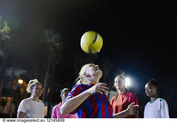 Young female soccer players practicing at night  heading the ball
