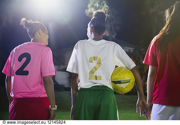 Young female soccer players with ball talking on field at night