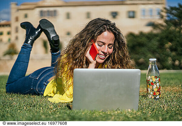 Young female speaking on smartphone on lawn