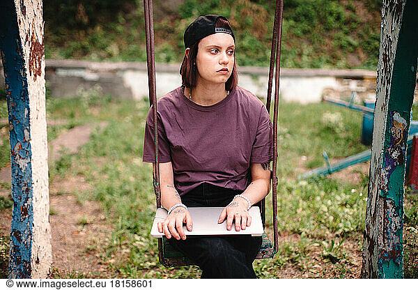 Young female student holding laptop sitting on a swing