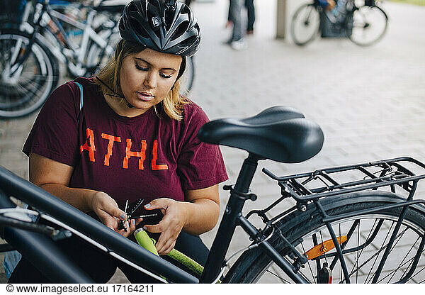 Young female student unlocking bicycle at parking station in university campus