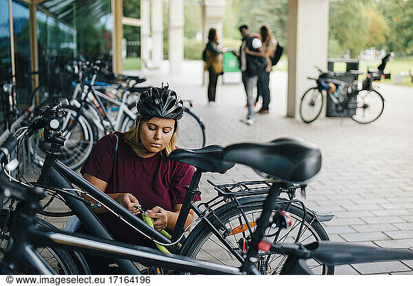 Young female student unlocking cycle at parking station in campus