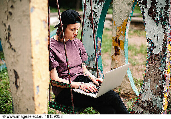 Young female student using laptop sitting on a swing