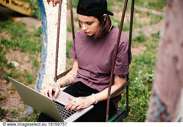 Young female student using laptop sitting on a swing