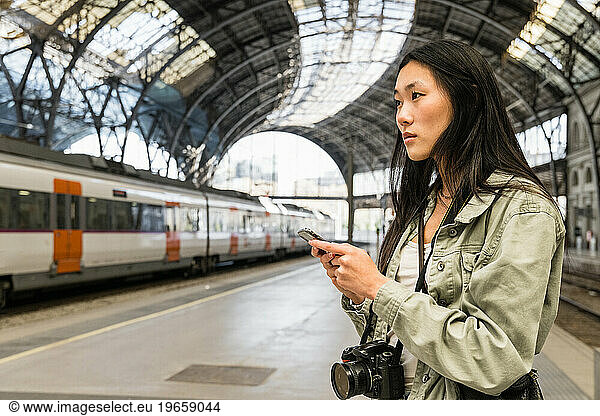 Young female traveler checking her phone in train station.