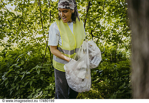 Young female volunteer with mouth open collecting plastics in park